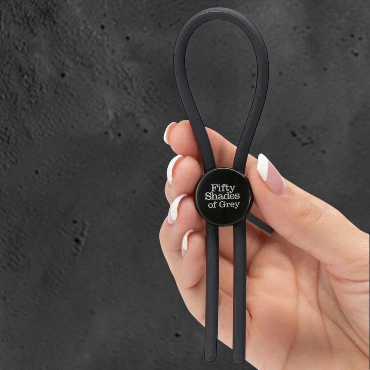 Anillo de placer ajustable de silicona negra de la colección Fifty Shades of Grey de PlayLoveToys sostenido en la mano