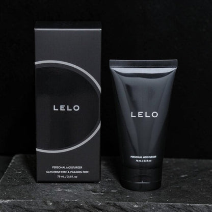 LELO Personal Moisturizer shown with its black retail box and matching squeeze tube on a dark textured surface against a black background.