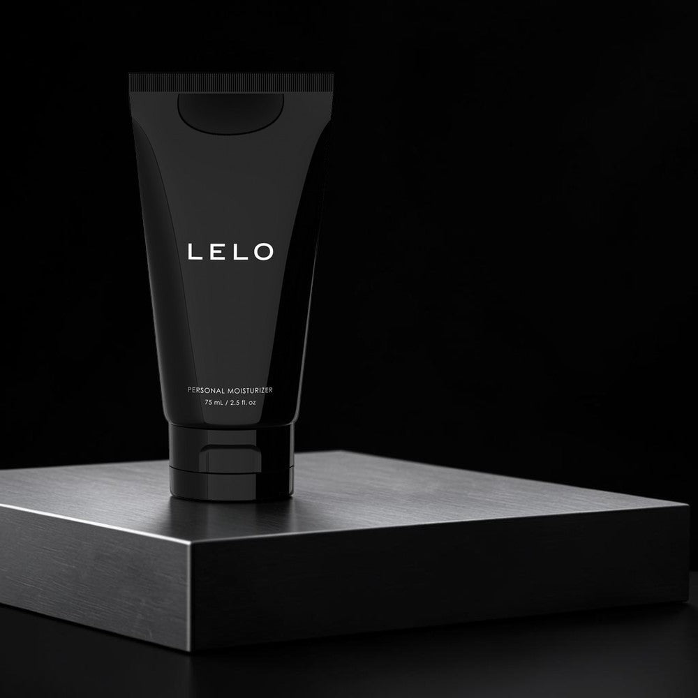 A black squeeze tube of LELO personal moisturizer stands upright on a dark metallic platform against a black background.