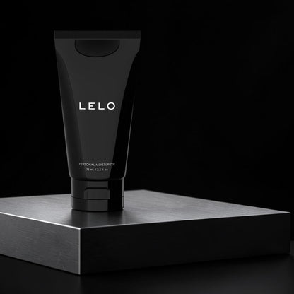 A black squeeze tube of LELO personal moisturizer stands upright on a dark metallic platform against a black background.