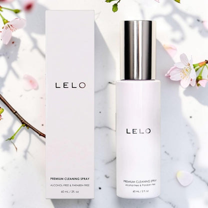LELO Premium Cleaning Spray bottle with a metallic silver cap next to its white packaging box, styled on a white marble surface with cherry blossom petals.