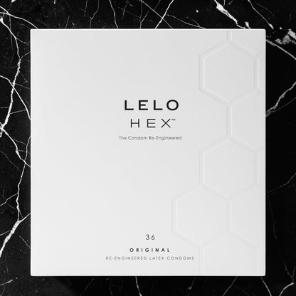 A square white product box for LELO HEX condoms, featuring black text and a subtle embossed hexagon pattern, set against a black marble background.