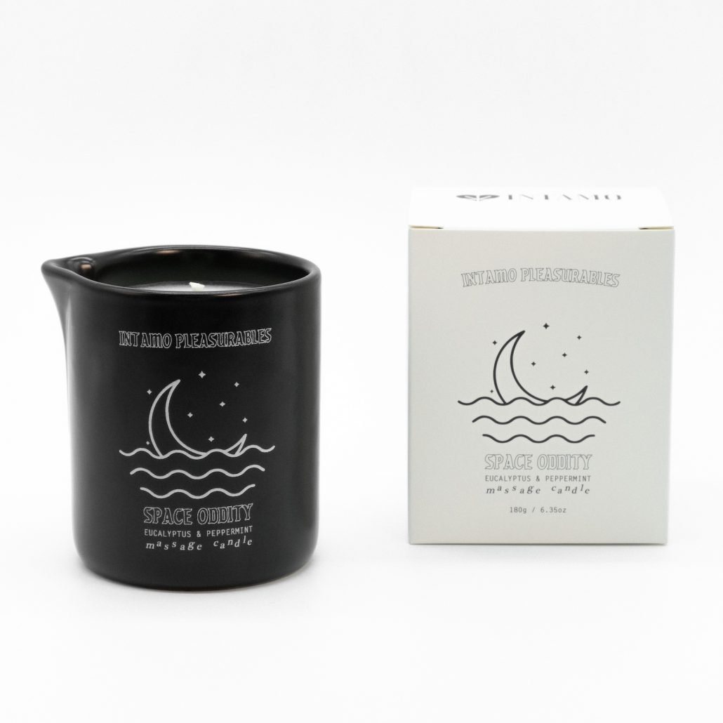 Black candle with moon and wave design next to its packaging on a white background
